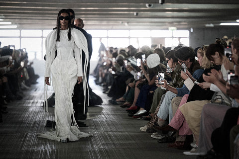 Models walking on a runway during a fashion show with an audience taking photos.